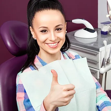 A woman in an exam chair holding a thumbs up